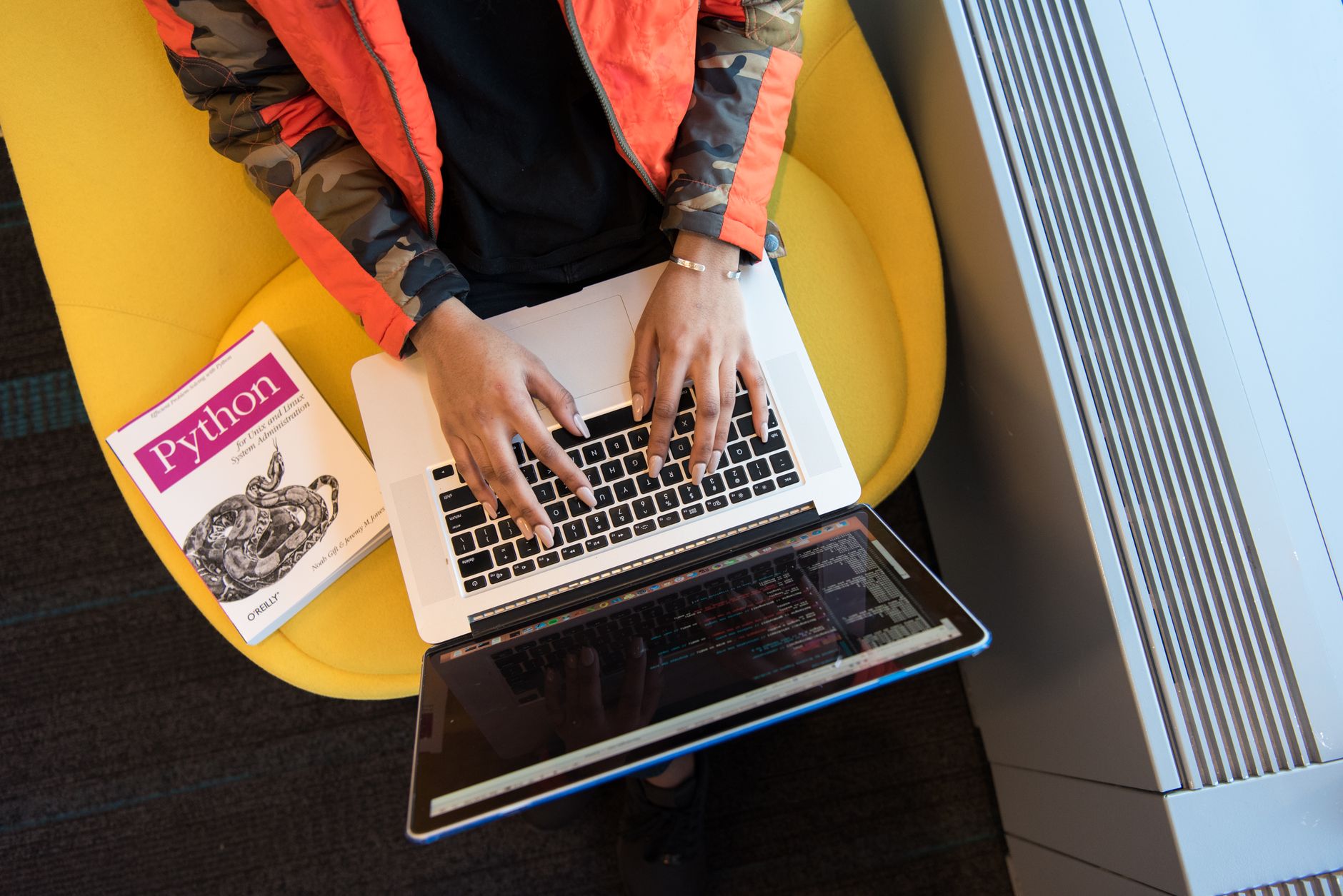 Kobieta programuje na laptopie obok książki o Pythonie