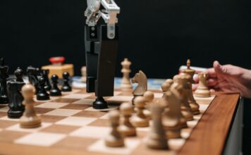 Historia sztucznej inteligencji: od prostych reguł do modeli generatywnych Ramię robota grające w szachy z człowiekiem, symbol rozwoju sztucznej inteligenc