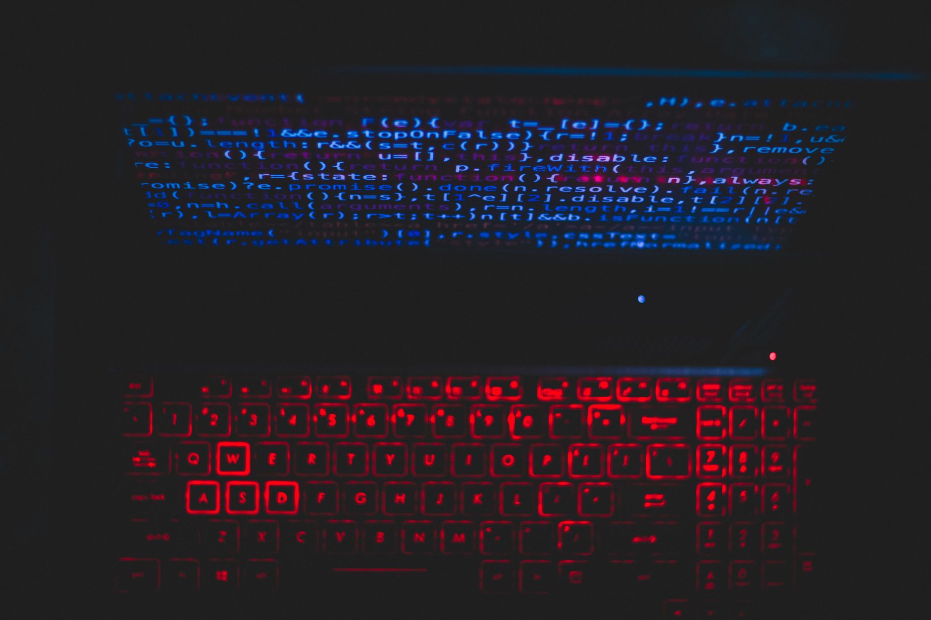 Laptop w ciemnym setupie z czerwonym podświetleniem i kodem na ekranie