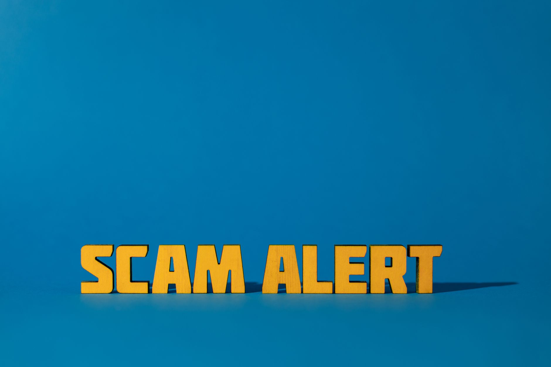 Napis Scam Alert na żółto na niebieskim tle ostrzegający przed oszustwem