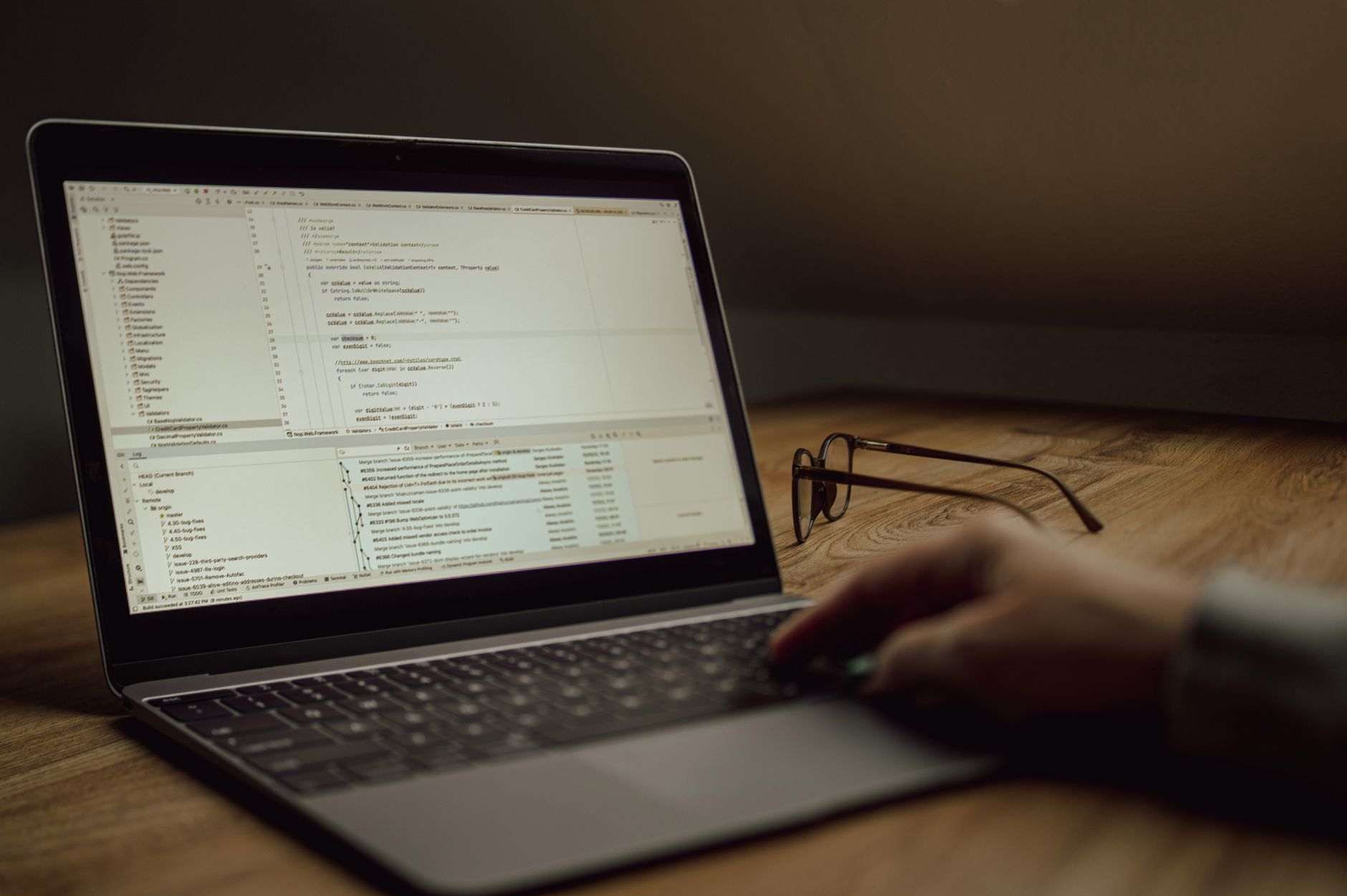 Osoba pracująca nad kodem na laptopie, okulary na stole